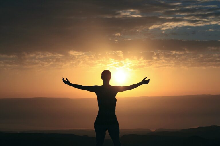 朝日に向かって両手を広げる人物のシルエット。継続する力と前向きな生き方をイメージした風景