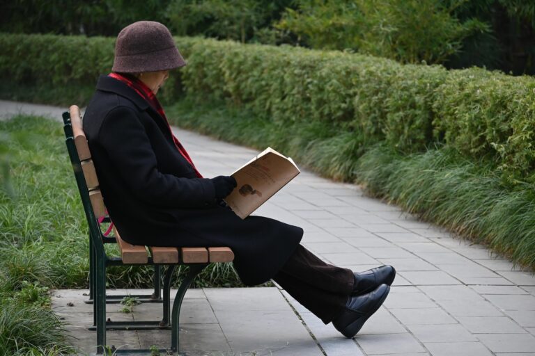 公園のベンチに座って本を読む女性