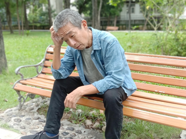 公園のベンチで頭に手を当て、仕事を辞めるかどうか考え込んでいる男性